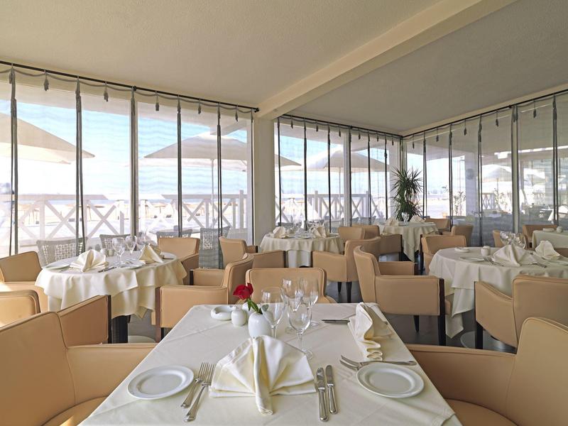 Jasna restauracja hotelowa z nakrytymi stołami i widokiem na taras z parasolami.