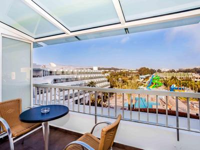 Balcony with two chairs and a table overlooking a pool and additional buildings.