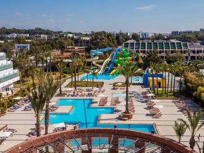 Grand espace piscine avec toboggans aquatiques, transats et bâtiments d'hôtel en arrière-plan.