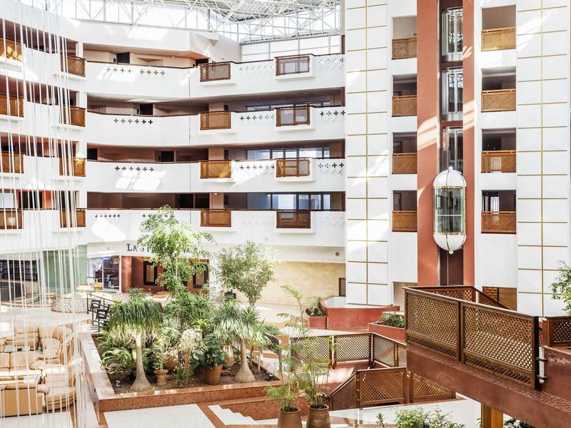 Interieur van een hotel met meerdere verdiepingen, ramen, balkons en een groen atrium.