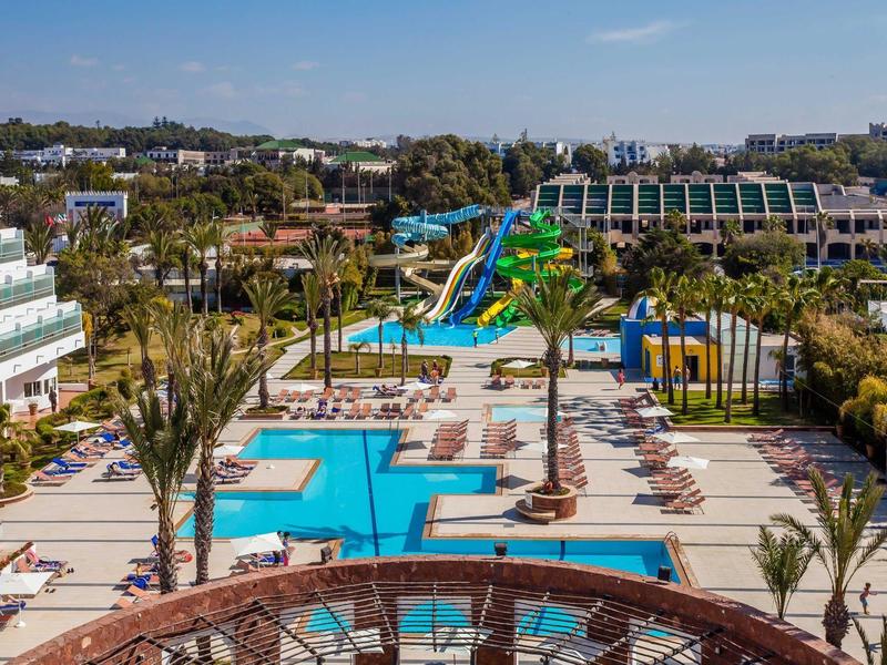 Groot zwembadgebied met glijbanen, ligstoelen en hotelgebouwen op de achtergrond.