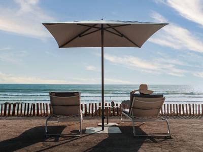 Zwei Liegestühle unter einem Sonnenschirm am Strand mit Blick auf das Meer.