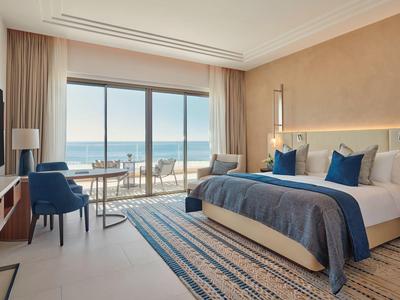 Hell eingerichtetes Hotelzimmer mit großem Bett und Balkon mit Meerblick.