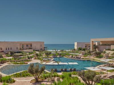 Moderner Hotelkomplex mit Poollandschaft und Blick auf das Meer unter klarem Himmel.