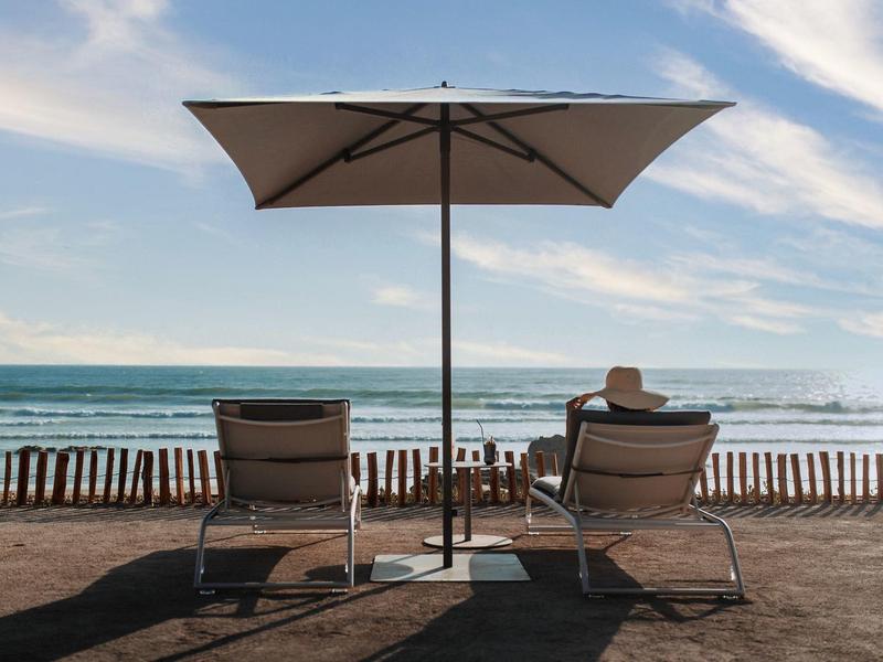 Twee ligstoelen met een grote parasol op een strand met uitzicht op zee.