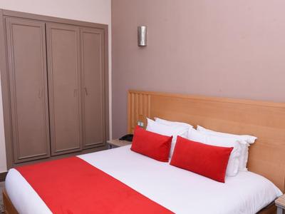 Schlafzimmer mit Doppelbett, rotem Bettläufer und Kissen, Holzkopfteil und grauem Kleiderschrank.