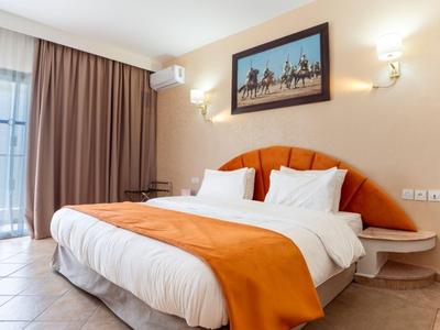 Gemütliches Hotelzimmer mit Doppelbett, orangefarbener Tagesdecke und geräumigem Fenster mit Vorhängen.