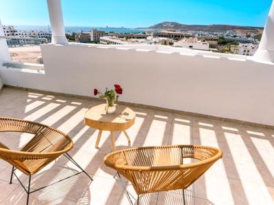 Balkon mit zwei Körbestühlen, kleinem runden Tisch und Stadtblick bei Sonnenschein.