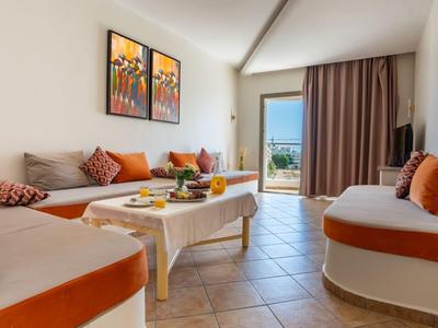 Ein heller Hotel-Wohnbereich mit weißen Möbeln und orangefarbenen Kissen, Terrasse mit Meerblick.