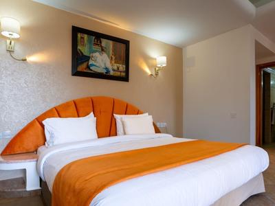 Gemütliches Hotelzimmer mit Doppelbett, orangefarbener Bettdecke und moderner Beleuchtung.