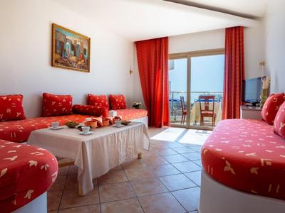 Helles Wohnzimmer mit roten Polstermöbeln, Fliesenboden und Balkon mit Meerblick.