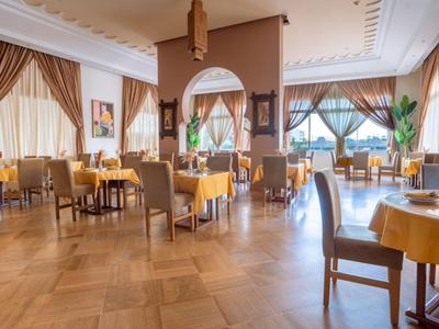 Helles Restaurant mit gelben Tischdecken und braunen Stühlen, großen Fenstern und Parkettboden.