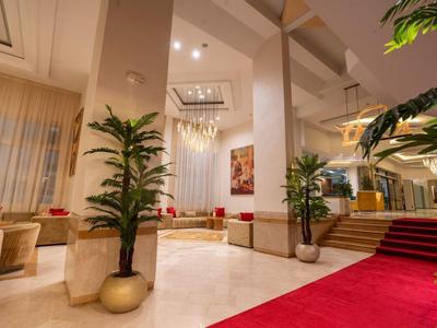 Elegante Hotellobby mit roten Teppichen, Pflanzen in goldenen Töpfen und moderner Beleuchtung.