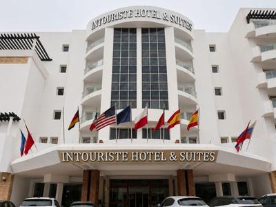 Großes weißes Hotelgebäude mit mehreren Flaggen und Autos vor dem Eingang.