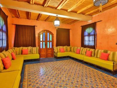 Soggiorno luminoso con divani gialli, cuscini colorati e tappeto decorato sotto soffitto con travi in legno.