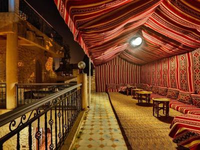 Lounge esterna serale con cuscini decorati e tappeti sotto una tenda a righe.