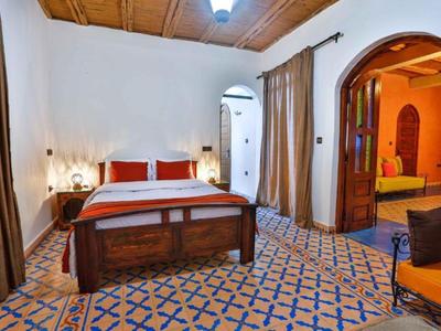 Camera da letto con letto in legno, pavimento decorato e accesso a una stanza adiacente.