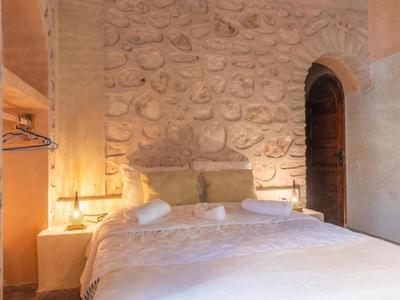 Camera d'albergo ben illuminata con parete in pietra naturale e letto matrimoniale con lenzuola bianche.