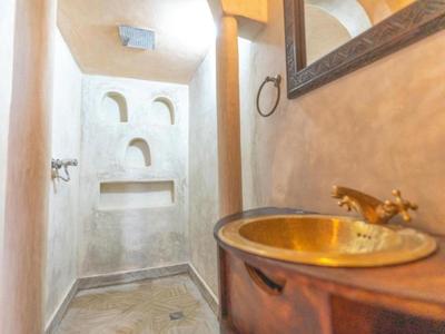 Piccolo bagno con area doccia, specchio rotondo e lavabo color ottone.