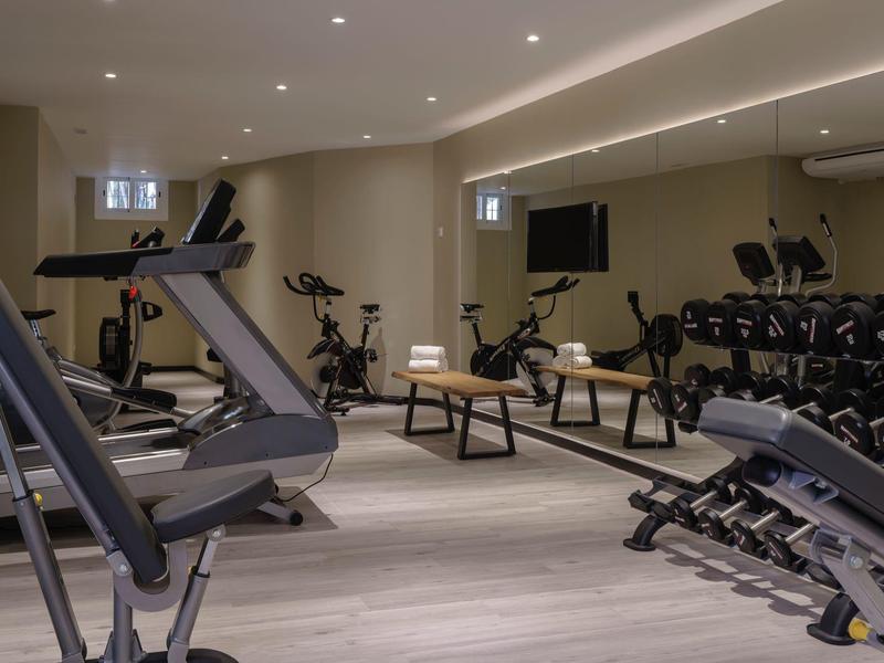 Moderner Trainingsraum mit Laufbändern, Hantelbank, Fahrradergometer und großen Spiegelwänden.