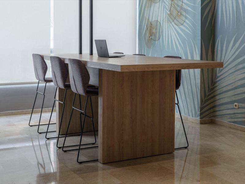 Moderner Holztisch mit vier hohen Stühlen, helle Räume, graue Wand mit Palmenmuster im Hintergrund.