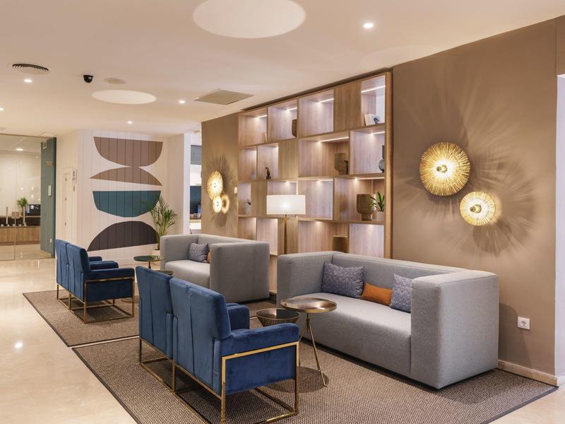 Moderner Lounge-Bereich mit grauer Couch, blauen Sesseln, Holzregal und dekorativen Wandlichtern.