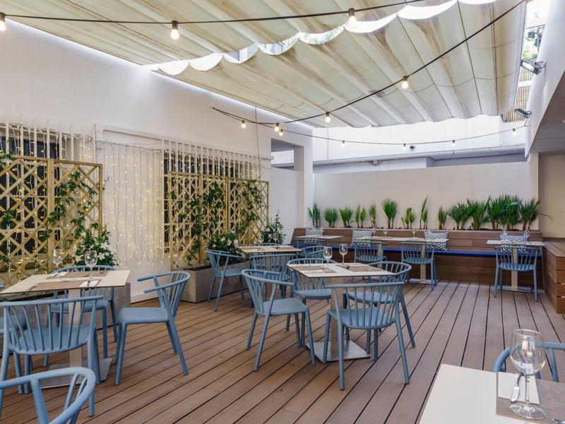 Moderner, heller Sitzbereich mit blauen Stühlen, Holzboden und grünen Pflanzen an den Wänden.