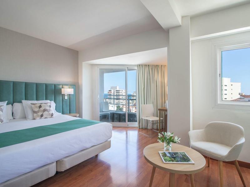 Modernes Hotelzimmer mit großem Bett, Holzfußboden, Balkon und hellen Möbeln.