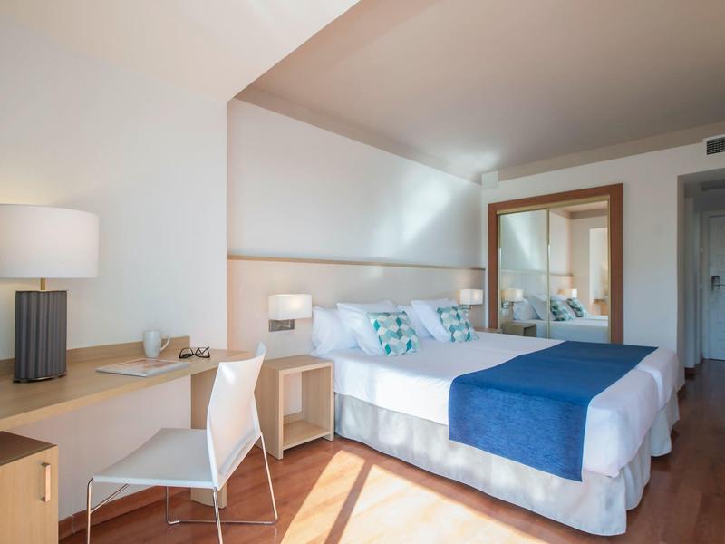 Modern eingerichtetes Hotelzimmer mit Doppelbett, blauem Bettläufer und großem Spiegel an der Wand.