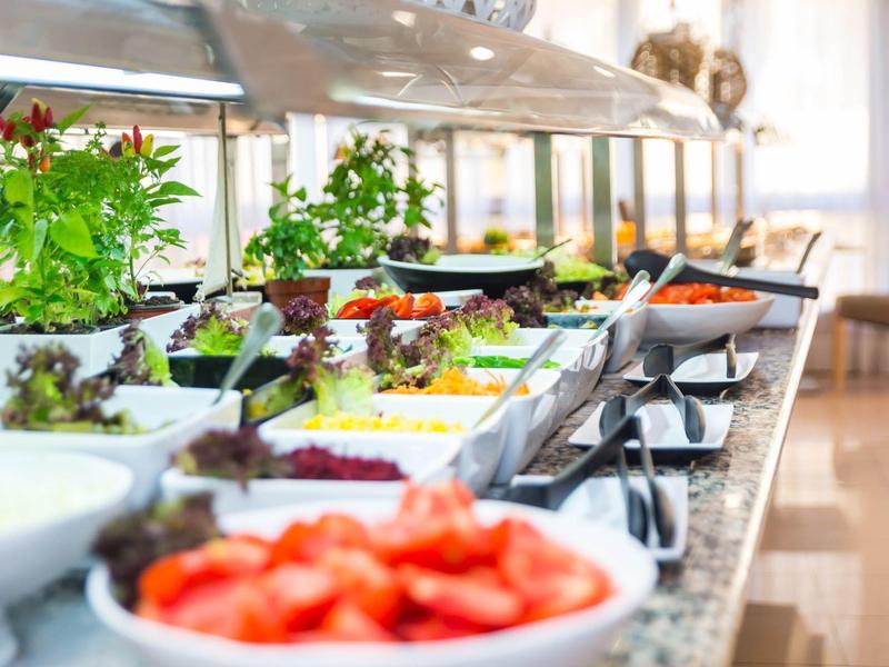 Buffet mit frischen Salaten, Gemüse und Kräutern in weißen Schalen auf hellem Tisch.