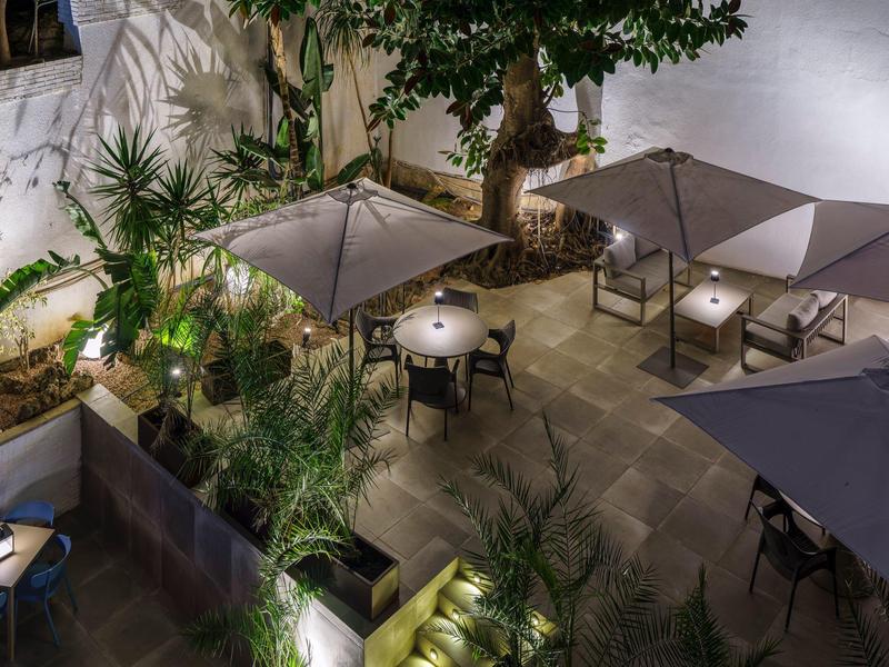 Gemütlicher Außenbereich mit Tischen, Stühlen, Sonnenschirmen und grünen Pflanzen bei Nacht.