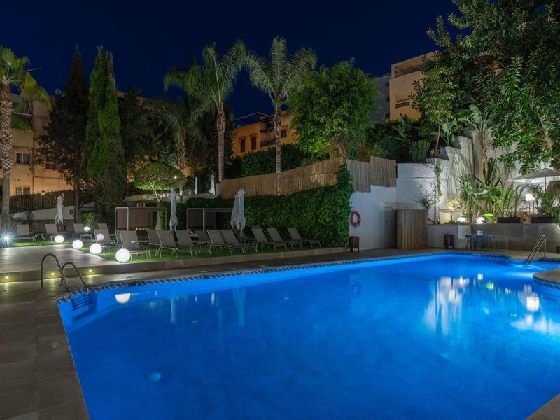 Beleuchteter Pool im Garten bei Nacht mit Bäumen und beleuchteten Sitzbereichen im Hintergrund.