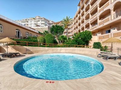 Ronde buitenzwembad met ligstoelen en hotelgebouwen onder een heldere hemel.