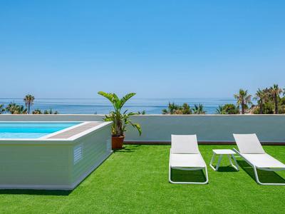 Twee ligstoelen naast een zwembad met uitzicht op zee en groen gras.