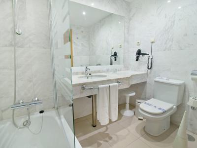 Lichte badkamer met marmeren wanden, badkuip, wastafel en toilet.