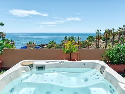 Whirlpool auf Terrasse mit Blick auf das Meer und Palmen im Hintergrund.