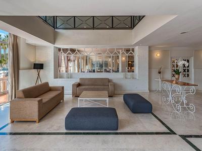 Lichte hotelontvangst met bank, blauwe poefs en elegante zithoek bij het raam.