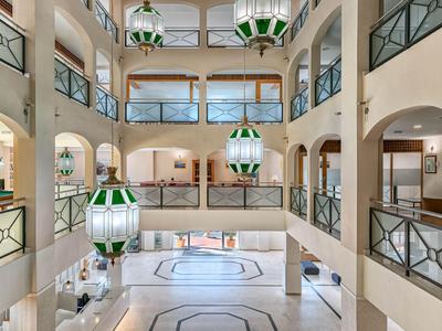 Helles Hotelfoyer mit balustradenartigen Geländern und grünen Hängelampen.