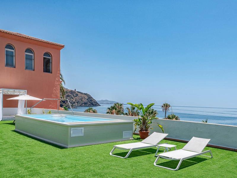 Terras met zwembad, ligstoelen en zeezicht op een zonnige dag.