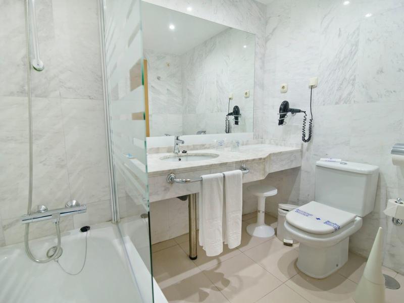 Lichte badkamer met marmeren wanden, badkuip, wastafel en toilet.