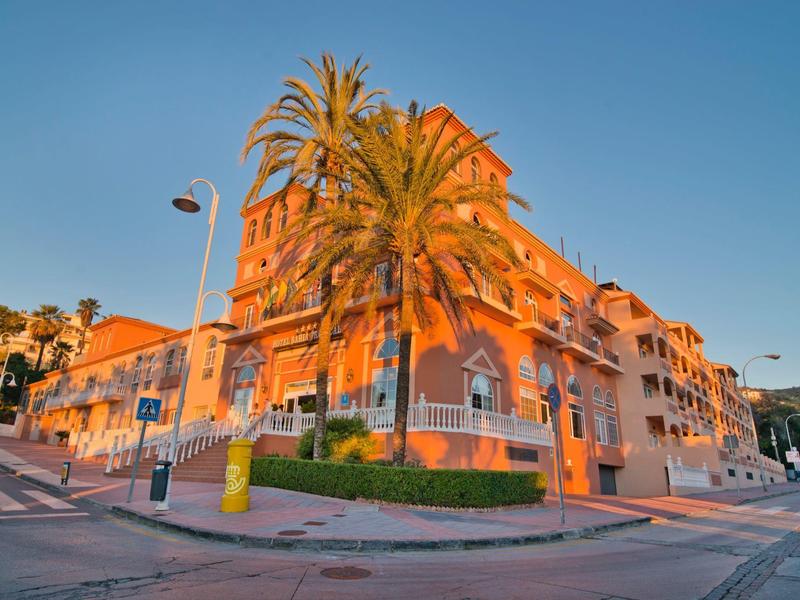 Een meerlaagse hotelgebouw met palmbomen bij zonsondergang op een hoek van de straat.