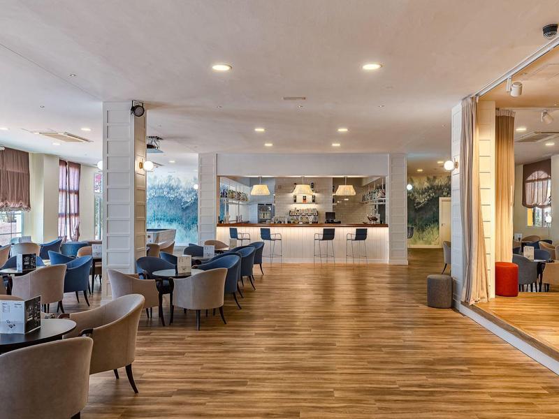 Lichte hotel eetruimte met houten vloer, tafels, stoelen en grote buffetbalie.