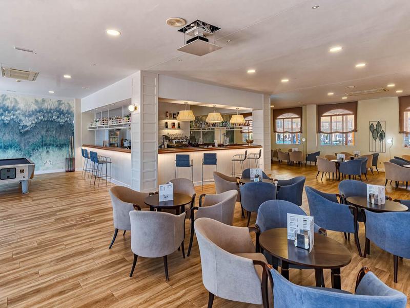 Moderne lounge met blauw-grijze stoelen, houten vloer en bar op de achtergrond.