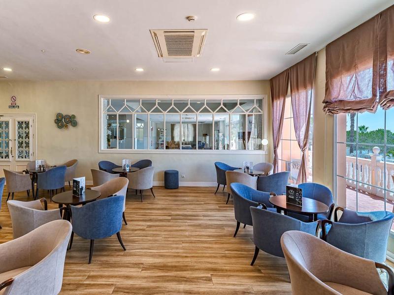 Modern restaurant met houten vloer, blauwe stoelen en grote ramen met uitzicht op het water.