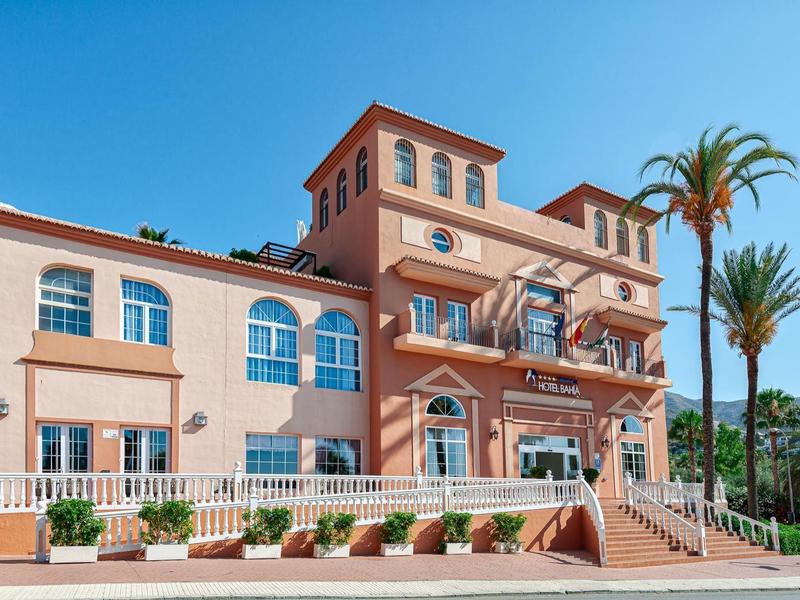 Een stijlvol hotel met terracotta verf en palmbomen onder een heldere blauwe hemel.