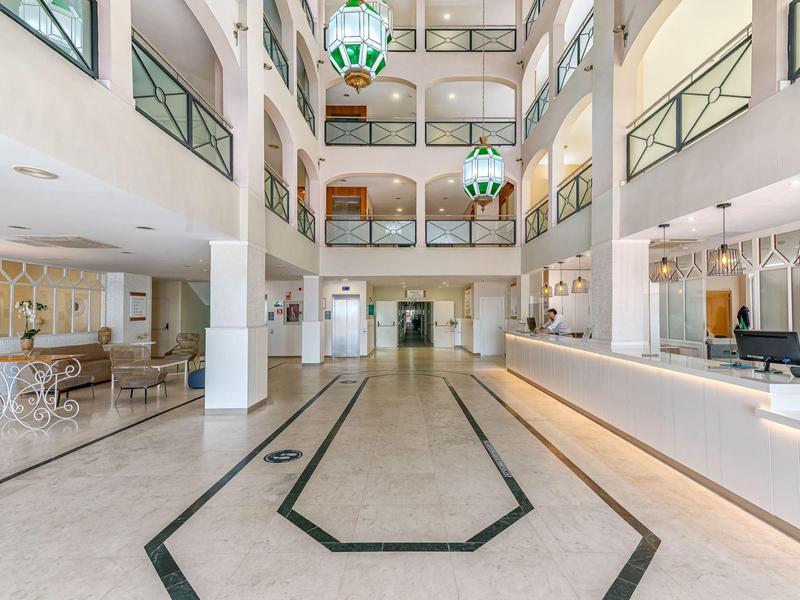 Lichte hotel lobby met receptie, meerdere verdiepingen, moderne hout- en marmerdecoratie.