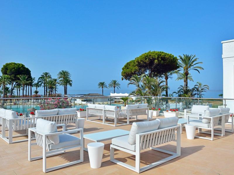 Ampia terrazza dell'hotel con mobili bianchi, vista sul mare e palme sotto un cielo azzurro.