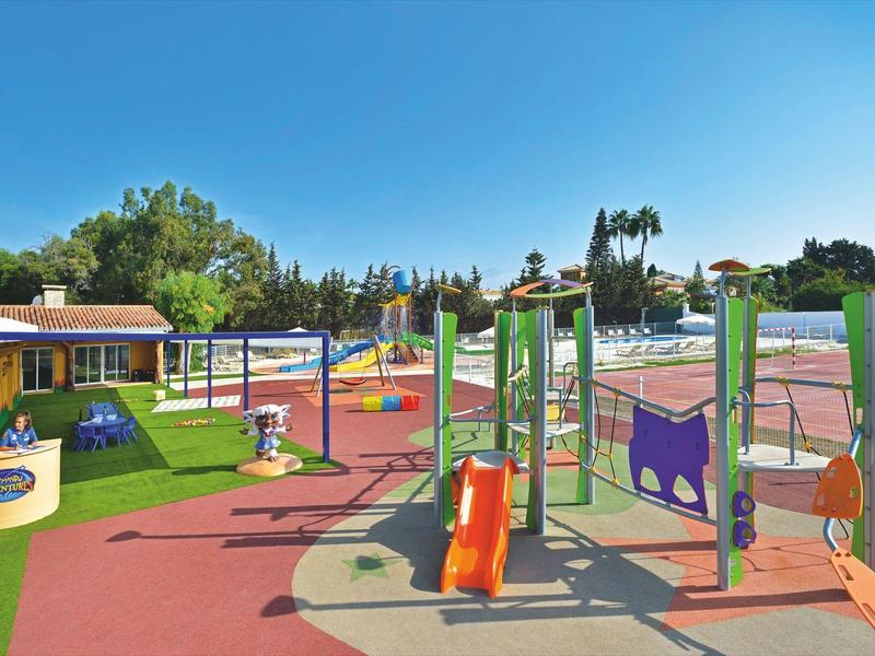 Area giochi esterna colorata con scivoli e altalene sotto un cielo blu chiaro.