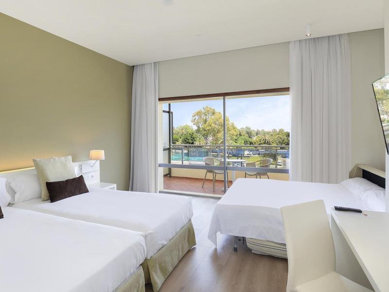 Camera d'hotel moderna con letti bianchi, grandi finestre e vista sulla natura.