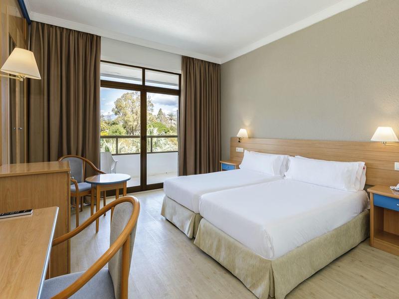 Camera d'hotel moderna con letto matrimoniale, balcone e mobili in legno chiaro.